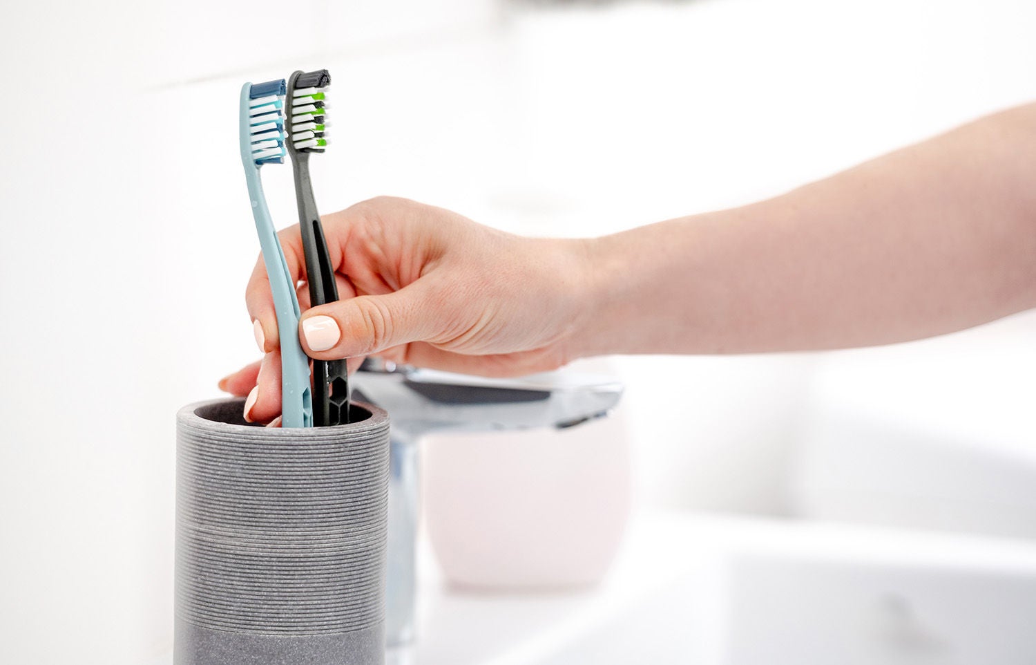 girls hand places two toothbrushes cup