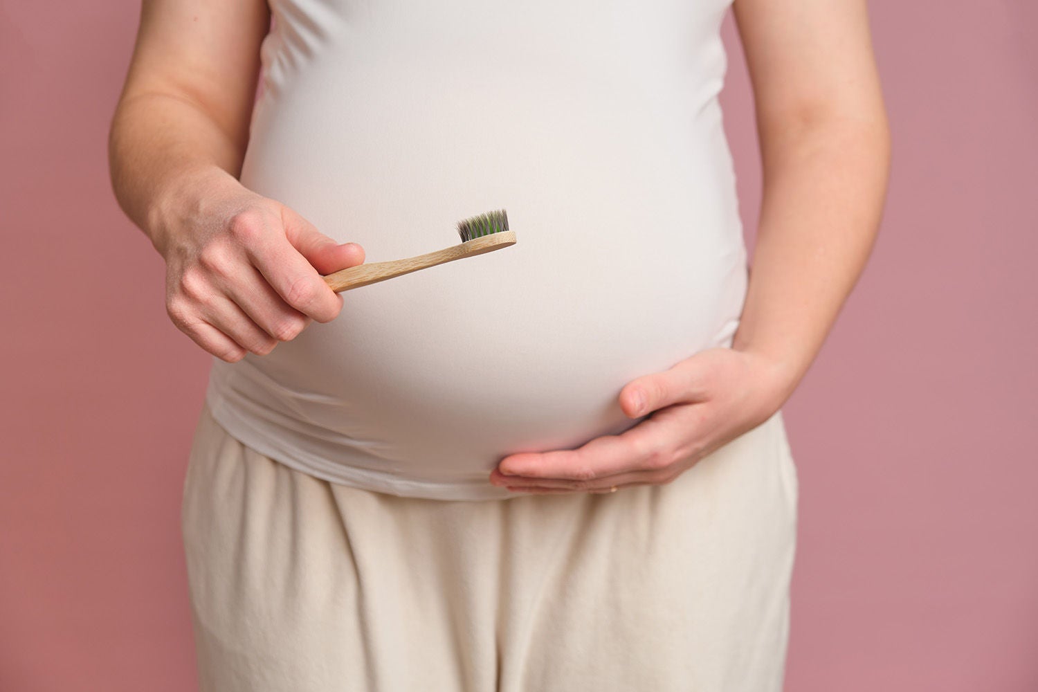 pregnant woman holding toothbrush studio pink